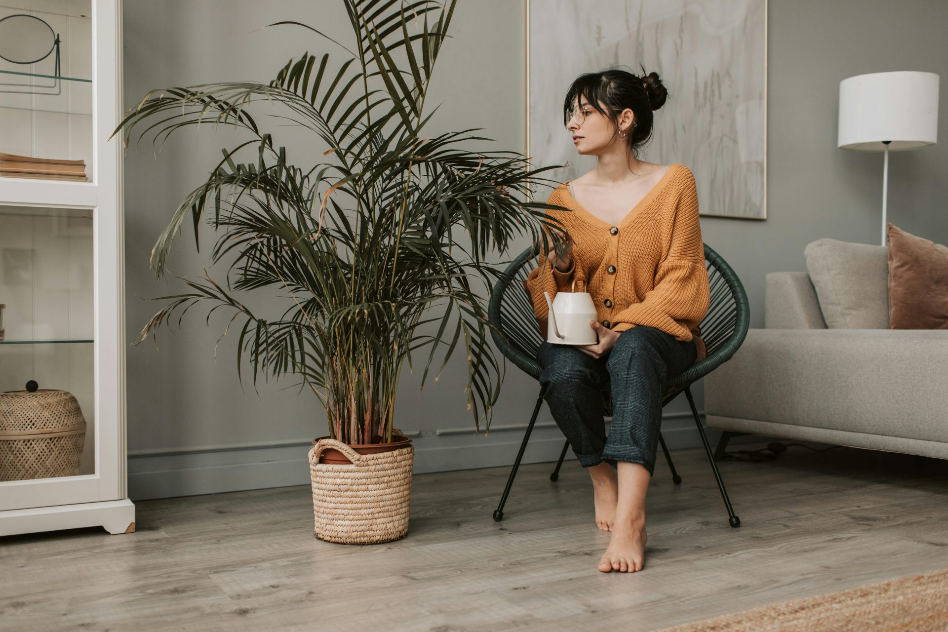Mujer sentada junto a una planta grande en un salón luminoso, con una taza en la mano