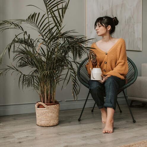 Mujer sentada junto a una planta grande en un salón luminoso, con una taza en la mano