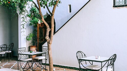 Pati interior amb arbres, taules d'exterior i una piscina allargada al costat d'una façana blanca