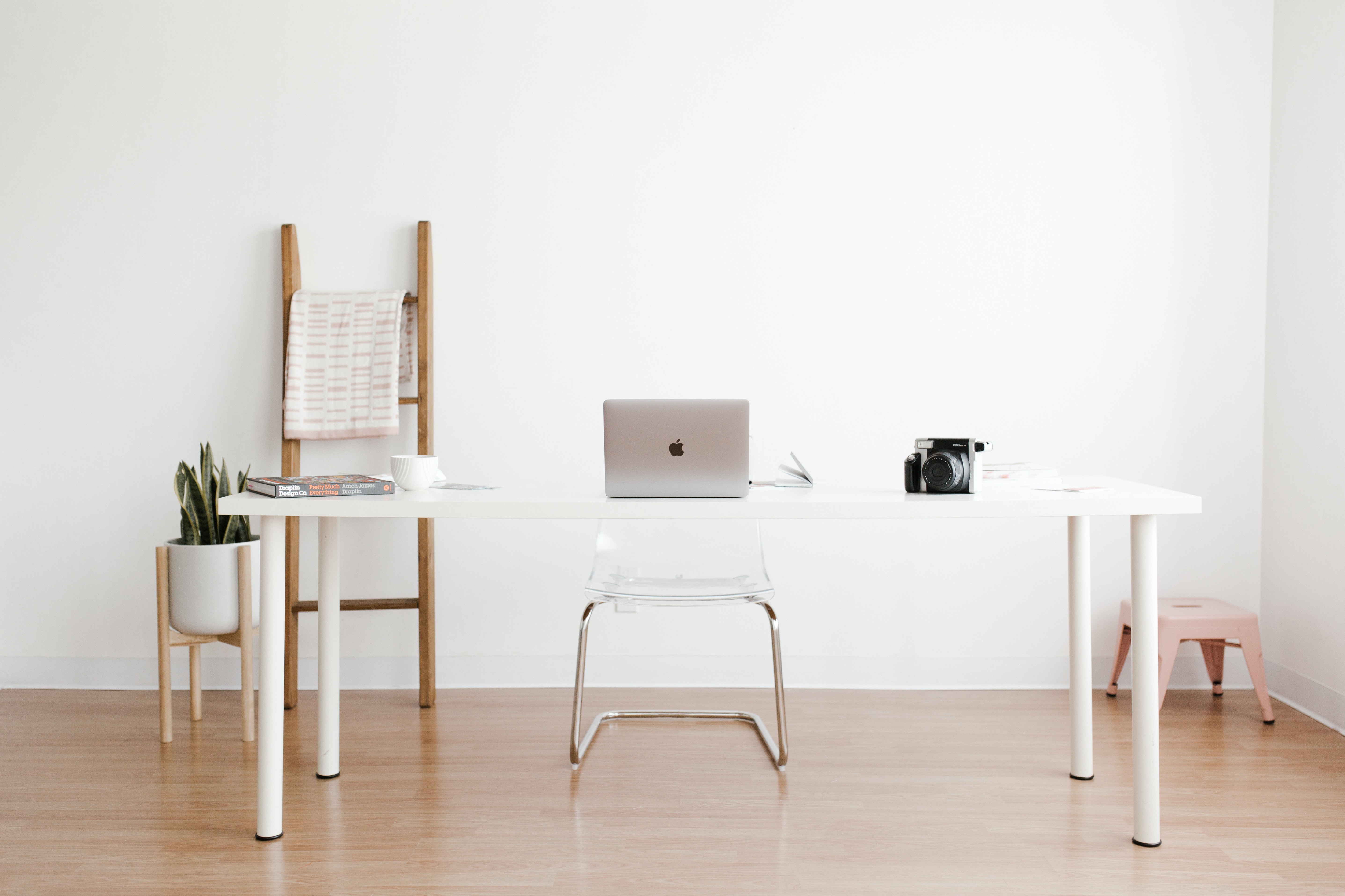 Escritorio blanco con un portátil abierto y una silla transparente, junto a una escalera decorativa de madera